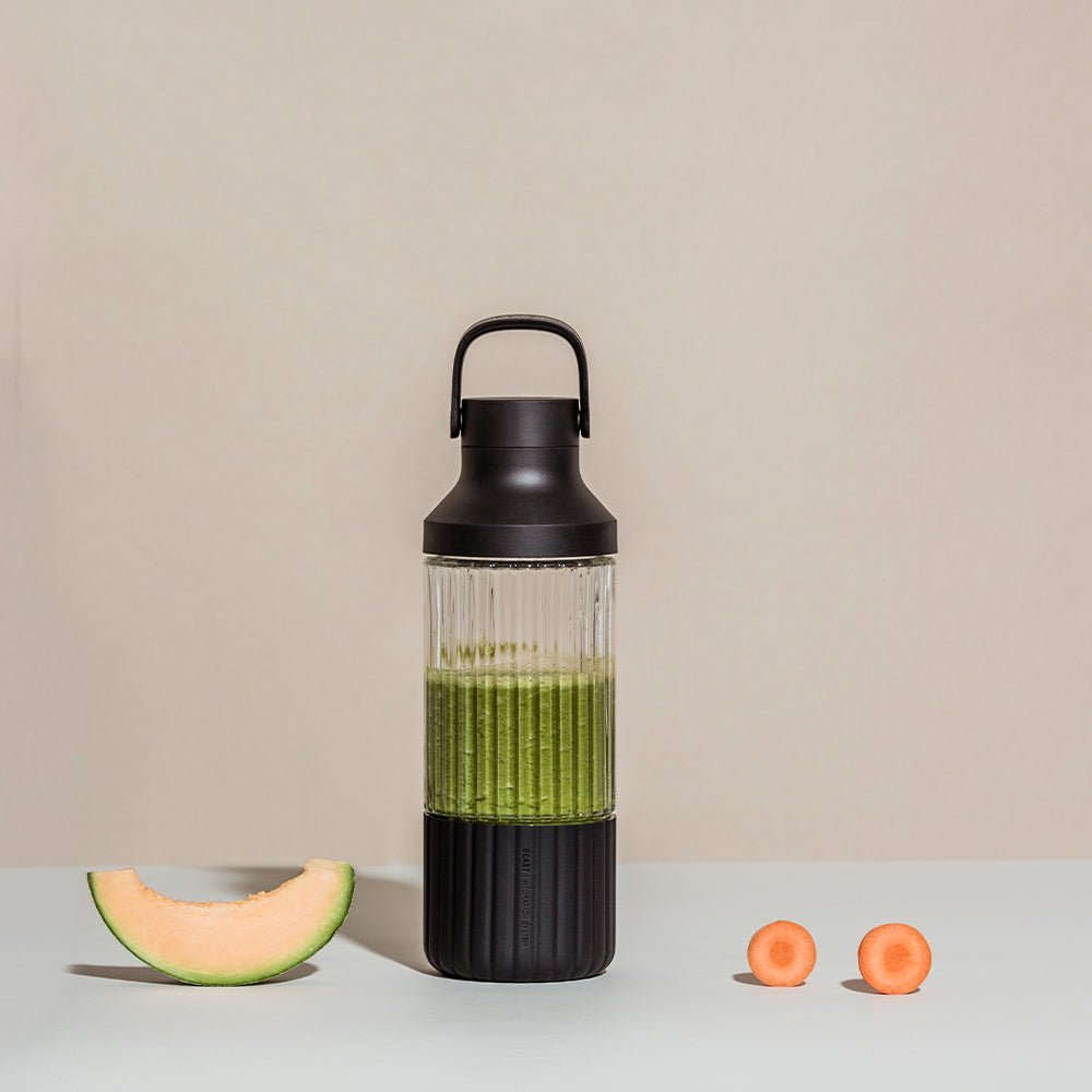 Beast Hydration Bottle | Carbon Black | Pebble Grey | Cloud White  Beast Hydration glass water bottle sitting on a white counter with a tan background with fruit next to it	